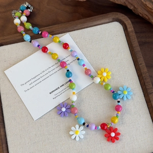 Macro shot of colorful beaded daisy necklace on a textured wooden tray with metal clasp