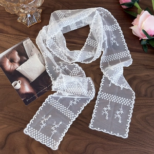 Close-up of white lace scarf with floral embroidery and scalloped edges on wooden desk