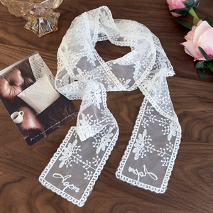 Detailed view of white floral lace scarf with embroidered script on a vintage wooden table