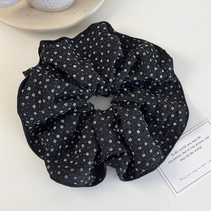 Dettaglio del grande elastico per capelli nero in seersucker con fiori bianchi su tavolo