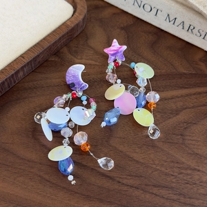 Detail of asymmetrical star and moon earrings with colorful crystal beads on wood