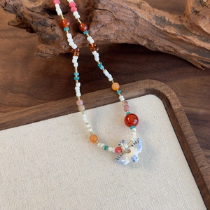 Gros plan d'un collier de perles colorées avec pendentif oiseau en céramique sur bois