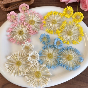 Detailed flat lay of colorful sunflower earrings in pink, yellow, and blue on white ceramic