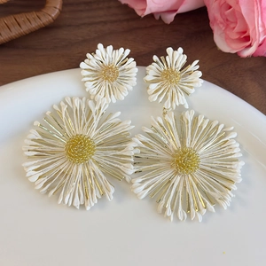 Detailed close-up of white sun flower earrings with golden core on a ceramic plate