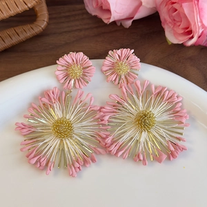 Close-up of pink and gold sunflower earrings with intricate woven metal flower details