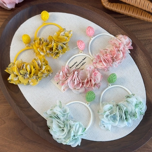 Detailed close-up of large bohemian fabric flower hoop earrings in yellow, pink, and green