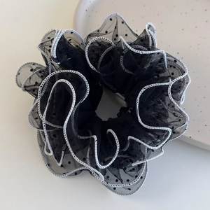 Close-up of black mesh polka dot scrunchie with white scalloped edges on ceramic plate
