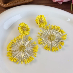 Detailed close-up of yellow daisy drop earrings on white ceramic plate with rustic background