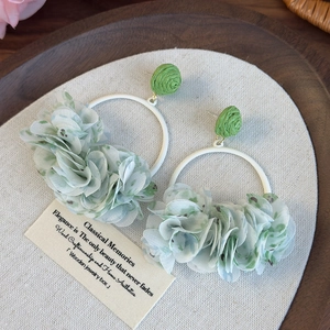 Close-up of floral fabric earrings with green chiffon petals on white metal rings
