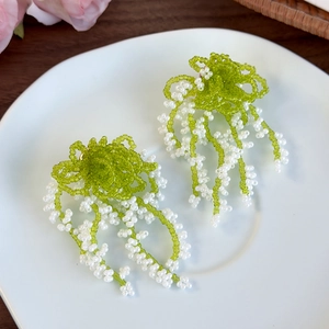 Detailed view of handmade lily of the valley beaded tassel earrings on a ceramic tray