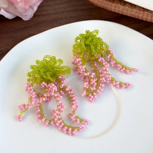 Handmade green and pink beaded fringe earrings displayed on a white ceramic plate