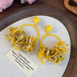 Macro detail of large yellow fabric floral petals and gold metal ring earring