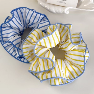 Minimalistische gestreifte Haargummis in Blau und Gelb auf einer dekorativen Muschelschale