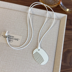 Detail shot of a white creative comb pendant necklace on a rustic beige linen texture background