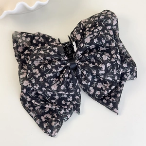 Detail der Haarklammer mit floralem Chiffon-Schleifen-Design und kleinen Blumen auf schwarzem Stoff