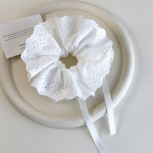 Close-up of white lace scrunchie with intricate embroidery and delicate satin ribbons