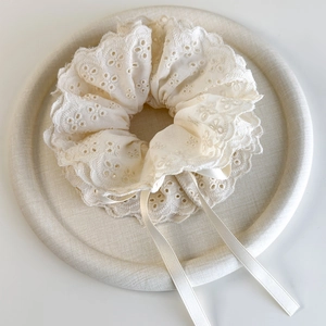 Close-up of cream lace scrunchie with floral embroidery and satin ribbons on a tray