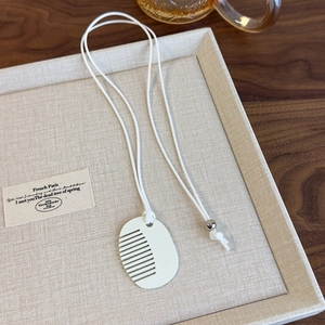 Detailed close-up of a white oval comb pendant on a woven cord necklace over a linen tray