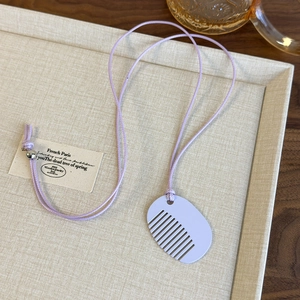 Detailed view of lavender comb-shaped pendant necklace with soft fabric cord on textured tray