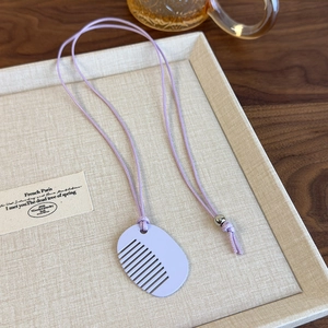 Detailed macro shot of a purple comb pendant and woven cord on a textured linen tray