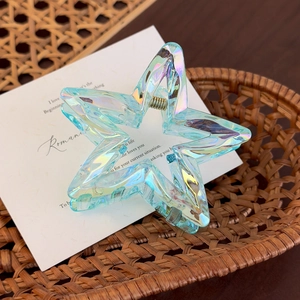 Detailed macro view of an iridescent star-shaped acrylic hair claw with golden metal spring