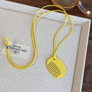 Macro shot of a vibrant yellow comb-shaped pendant on a minimalist woven cord necklace