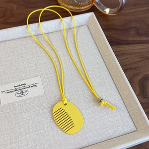 Detail view of a yellow comb pendant necklace with woven cord and silver bead accent