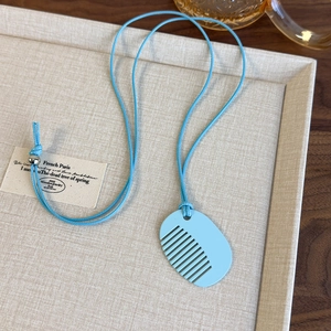 Close-up of a light blue comb-shaped pendant necklace on a beige display tray