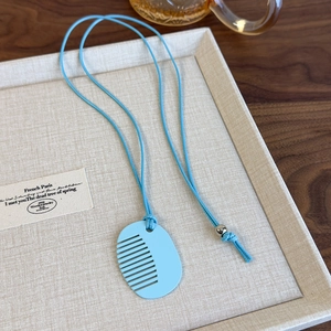 Close-up of a light blue comb-shaped acrylic pendant on a beige linen display tray