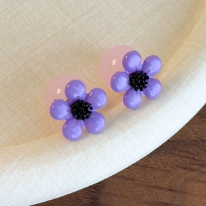 Macro detail of purple resin flower earrings with black stamen and pink translucent backing
