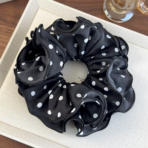 Detail of elegant black and white polka dot scrunchie with soft ruffled satin texture