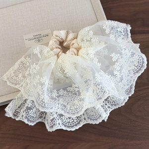 Détail d'un chouchou en satin beige avec broderie de dentelle florale blanche