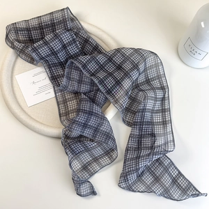 Detail of a sheer black and grey checkered skinny scarf displayed on a white tray