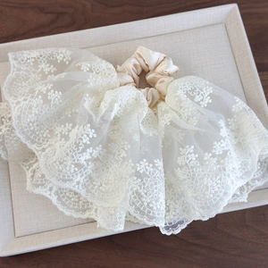 Gros plan d'un chouchou en dentelle beige avec broderie florale et plis en satin soyeux