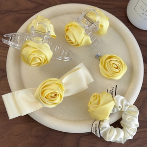 Detailed set of yellow satin rose hair clips and organza scrunchie on a round tray