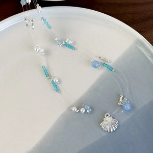 Detail of multi-strand beaded necklace with sea blue crystals and silver scallop charm