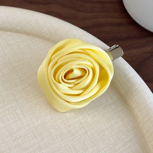 Detail of a handmade 3D yellow silk rose hair clip on a textured beige display tray