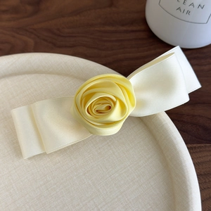 Detail view of a handmade cream ribbon bow with a yellow satin rose hair clip on a tray