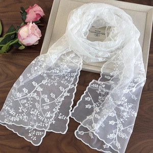 Détail de la broderie en dentelle florale blanche et des bords festonnés sur l'écharpe