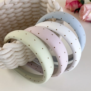 Détail de quatre serre-têtes en éponge à pois colorés rangés dans un panier rustique