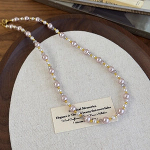 Détail de perles roses et cristaux sur un plateau en bois avec un fermoir mousqueton doré