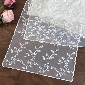 Gros plan sur une écharpe en dentelle blanche brodée avec des détails de fleurs et résille