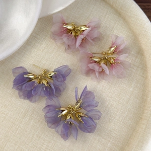 Floral tulle earrings with gold metal centers in soft pink and purple on a textured tray