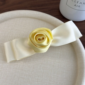 Close-up of handmade yellow 3D fabric rose and satin ribbon hair clip on woven tray