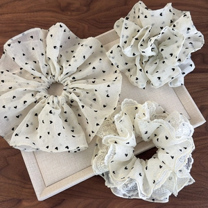 Three creamy white scrunchies with black heart patterns and delicate lace edges on tray