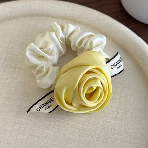 Detail of a cream satin scrunchie with a yellow fabric rose and branded ribbon