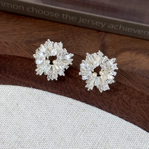 Detail of flower earrings with baguette zircons and white pearls on a dark wood background