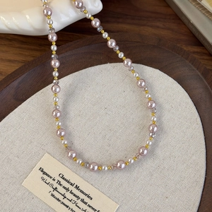 Détail du collier de perles roses et blanches avec touches dorées sur un plateau en bois