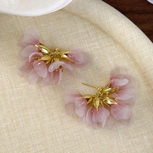 Close-up of pink tulle flower earrings with golden metal pistils on beige fabric