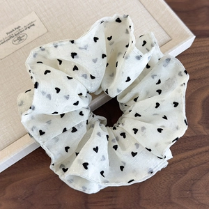 Detail of a creamy mesh scrunchie featuring black heart patterns and pleated soft textures